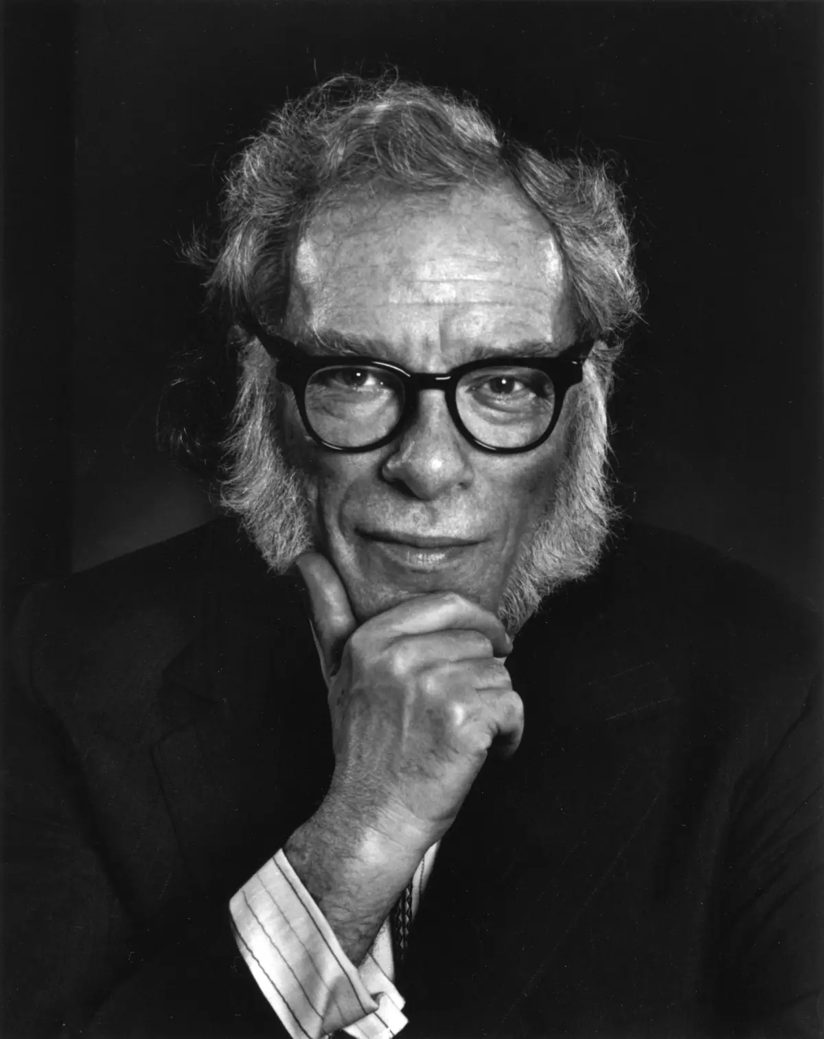 A black-and-white portrait of an older man with glasses and a beard, wearing a suit and resting his chin on his hand…