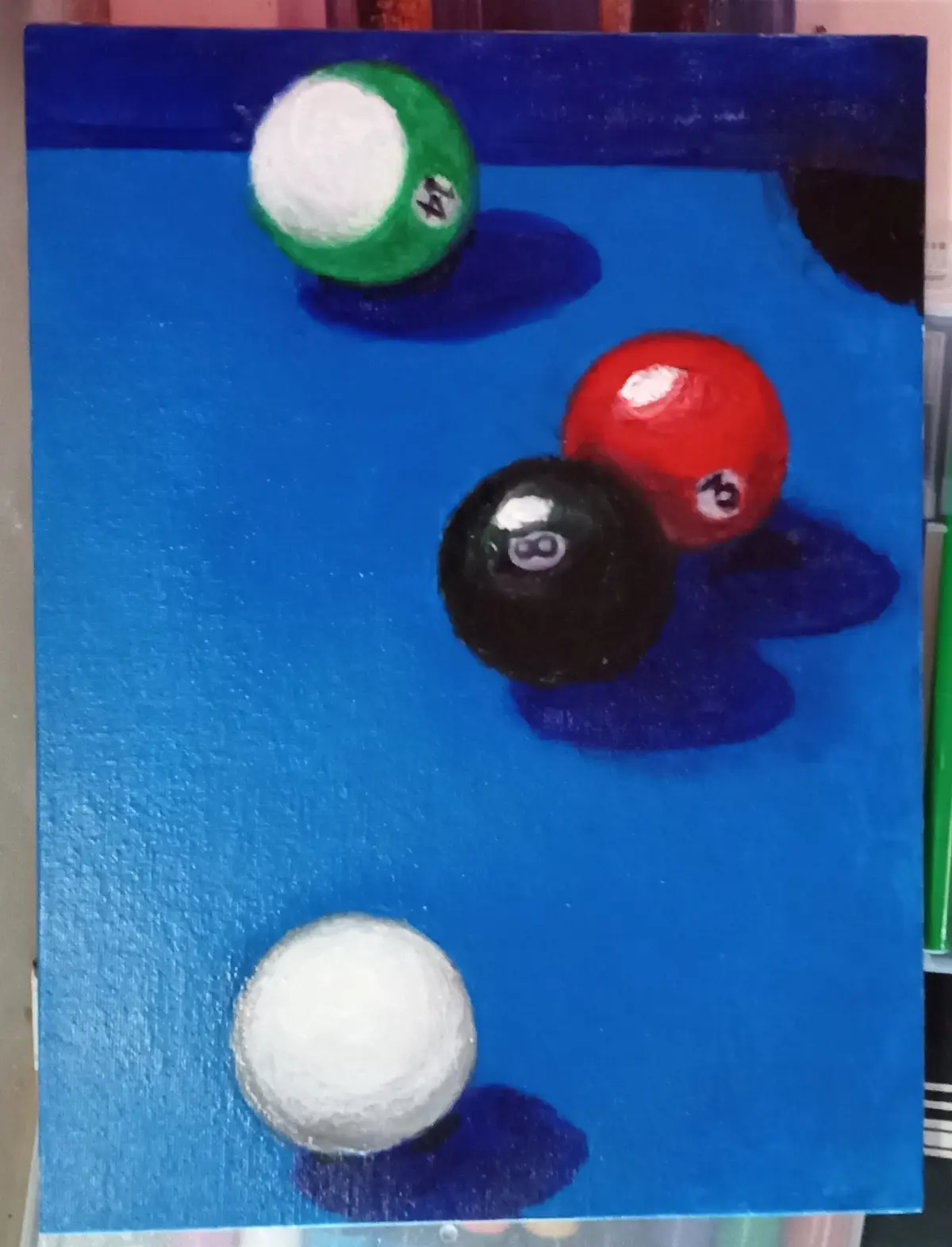 A painting depicts four pool balls on a blue surface: a green 4-ball, a red 6-ball, a black 8-ball, and a white cue ball…