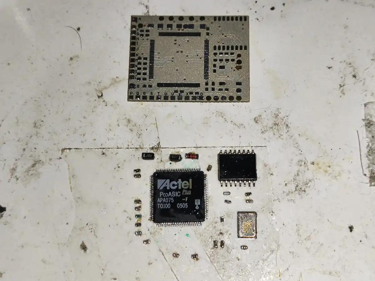 A close-up photo shows two circuit boards on a dirty white surface. The lower board features a prominent black Actel ProASIC…