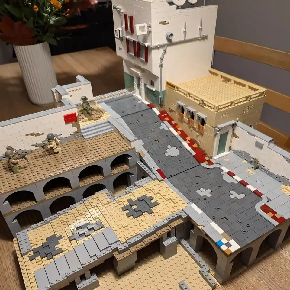 A detailed Lego cityscape with buildings, streets, and archways, featuring three Lego minifigures in military gear holding…