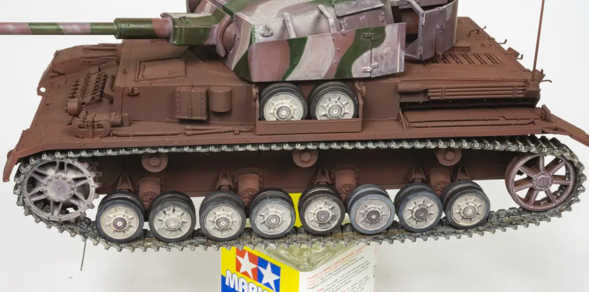 A detailed scale model of a military tank with a brown and green camouflage pattern is shown resting on its tracks atop a…