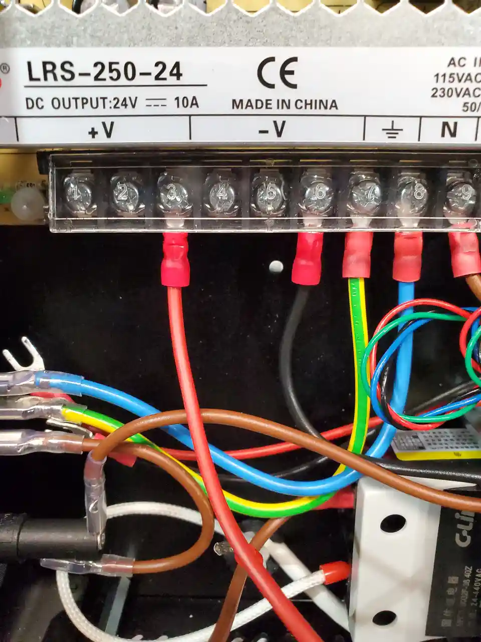 A close-up photo of a messy electrical terminal block with red, blue, green, and brown wires tangled together. The terminal…