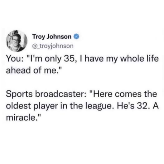 A screenshot of a tweet by Troy Johnson showing a humorous exchange where a person claims to have a long life ahead at age…