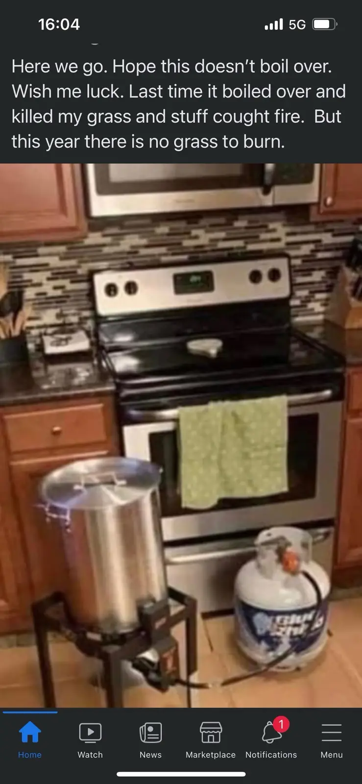 A large stainless steel pot sits on a portable burner connected to a propane tank in a kitchen, positioned in front of a…