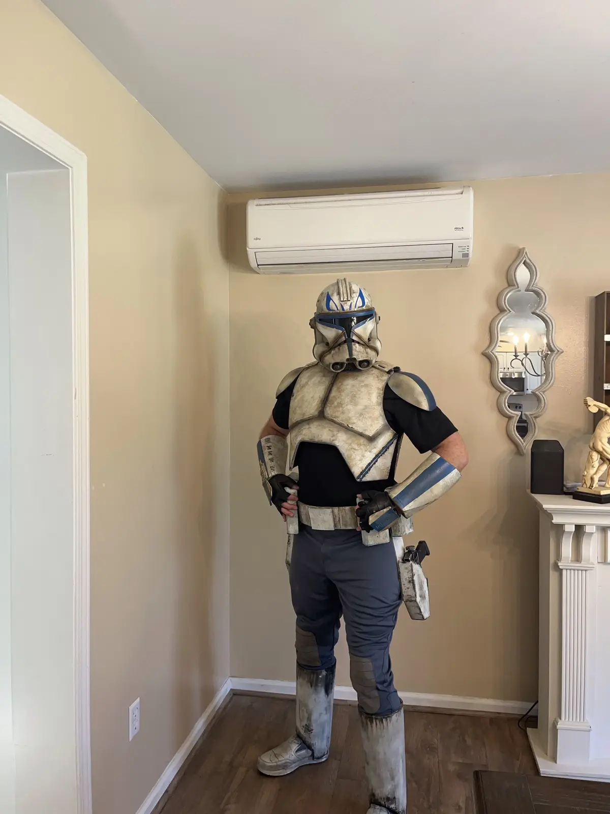 A person in a detailed, weathered Star Wars Clone Trooper costume stands indoors, hands on hips, directly beneath a white…