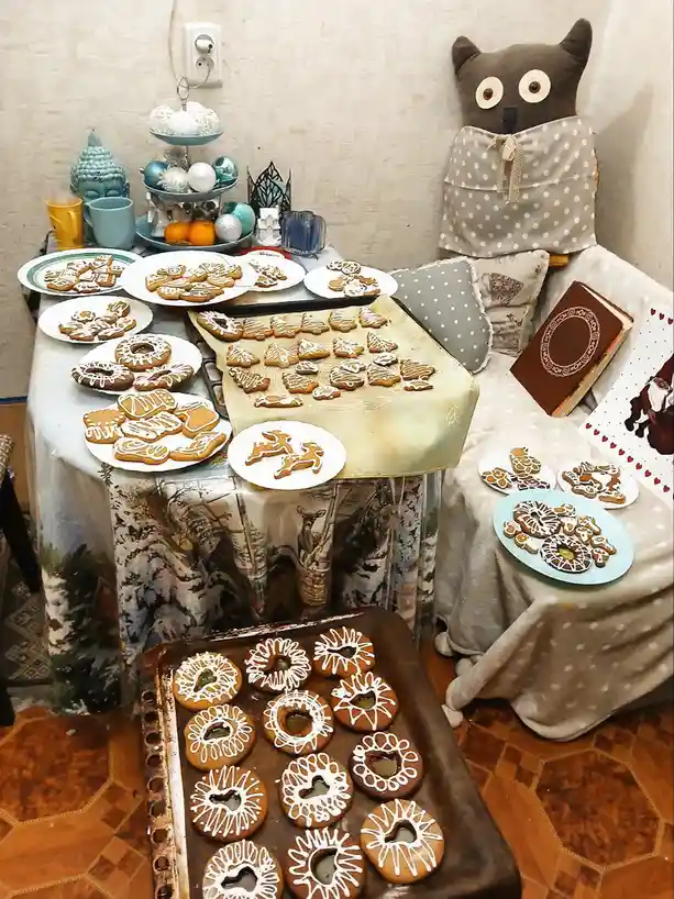 A cozy room displays numerous plates and trays of intricately decorated gingerbread cookies in various shapes like reindeer…