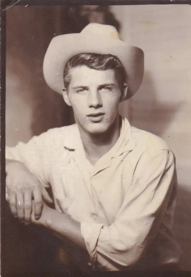 A vintage sepia-toned portrait of a young man wearing a cowboy hat and light-colored shirt, looking directly at the camera…