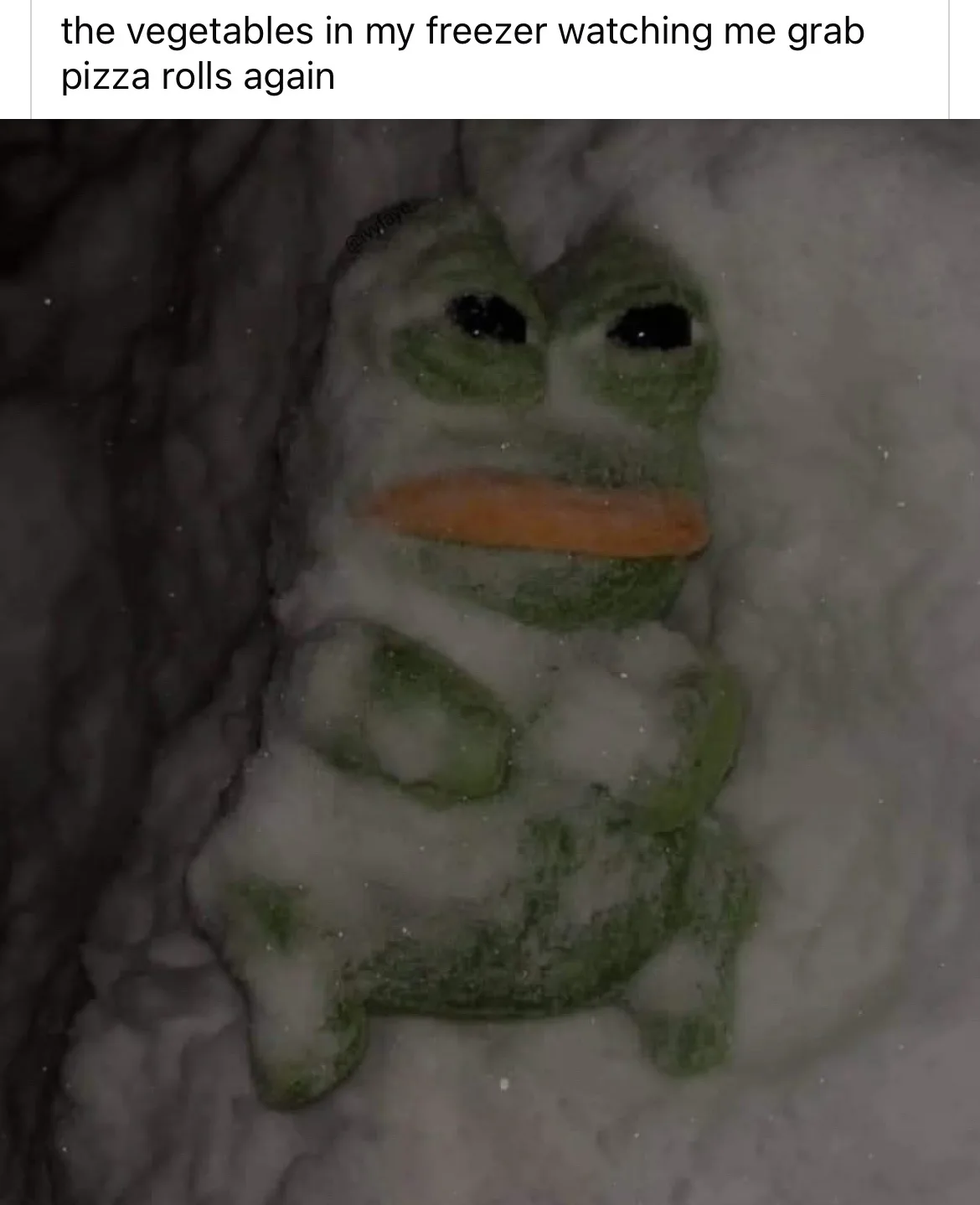A green, sad-looking Pepe the Frog plush toy is partially buried in snow, with a carrot stuck in its mouth as if it's a…