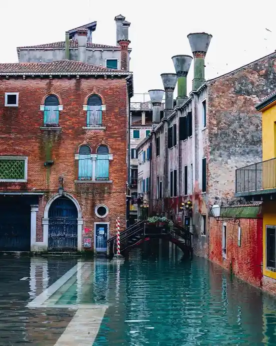 A photo of a flooded Venice canal with historic brick buildings on either side, water covering the street and reflecting the…