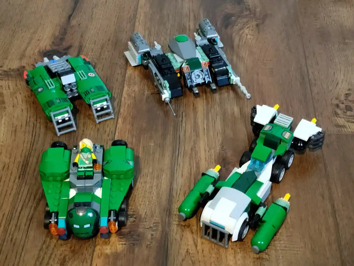 Four Lego Star Wars vehicles, mostly green and gray, are arranged on a wooden floor. One vehicle has a minifigure seated in…