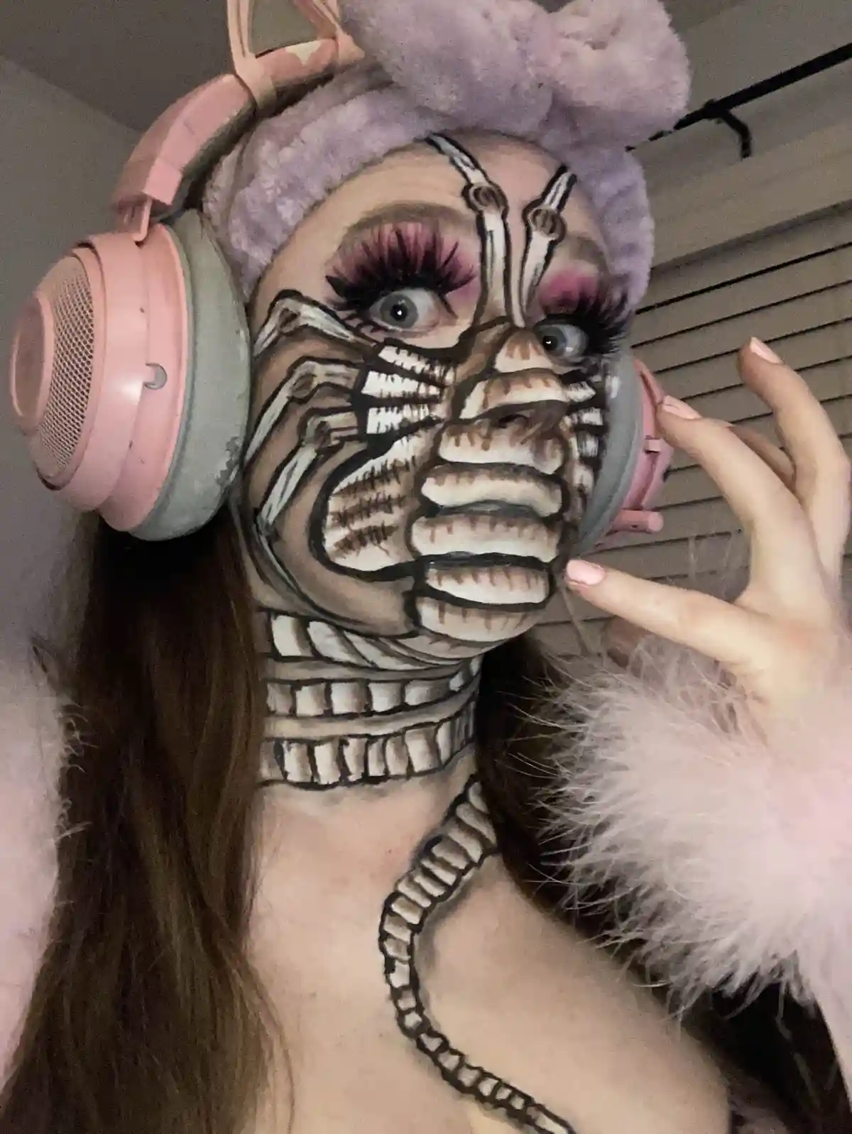 A person with elaborate face paint depicting a cybernetic or robotic face, complete with mechanical lines, exposed gears…