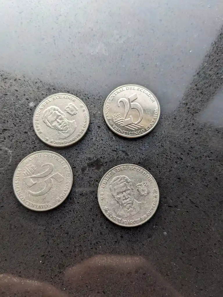 Four Ecuadorian coins are arranged on a dark speckled surface; two show the portrait of Jose Joaquin de Olmedo and two show…