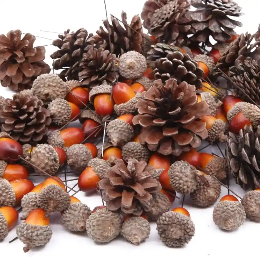 A pile of brown pinecones and orange acorns, each attached to thin wire stems, arranged against a plain white background…