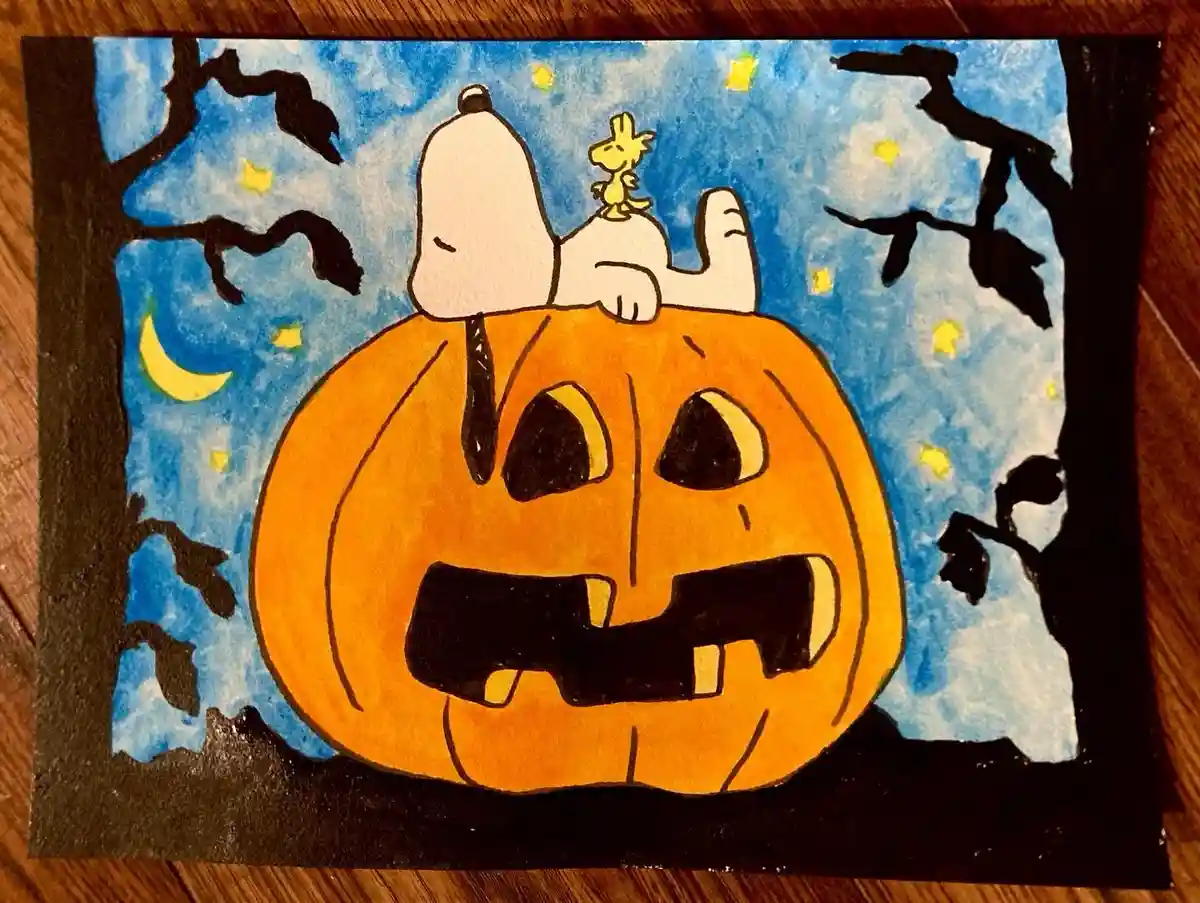 A hand-drawn Halloween scene shows Snoopy, the white beagle from Peanuts, lounging atop a large orange jack-o-lantern with a…