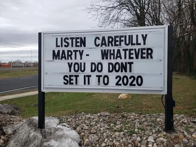 A white outdoor light-up sign with black lettering stands in a grassy area with gravel and rocks. The sign reads: 'LISTEN…