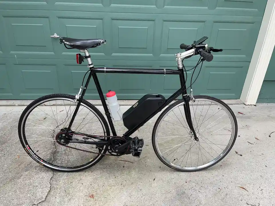 A black bicycle with a large black battery pack mounted on its frame, a water bottle, and a smartphone mounted on the…