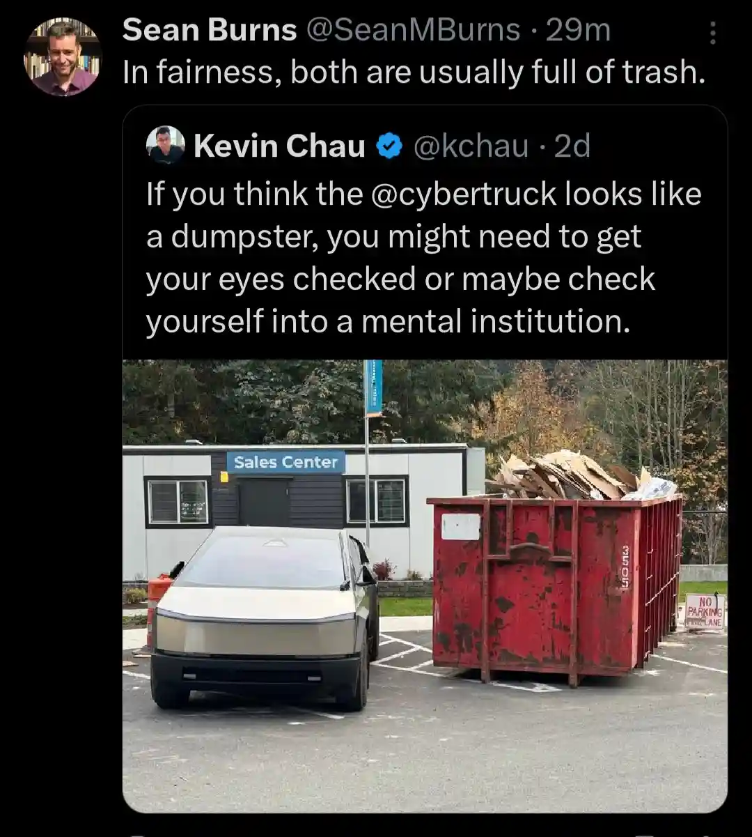 A silver Tesla Cybertruck is parked next to a large red dumpster overflowing with cardboard and debris in a parking lot. A…