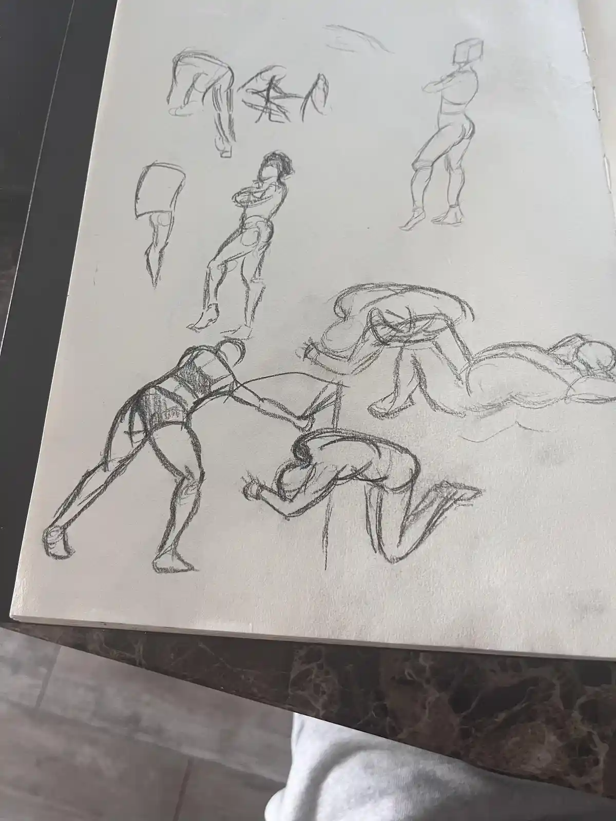 A sketchbook page filled with rough pencil drawings of human figures in various poses, including some distorted or…