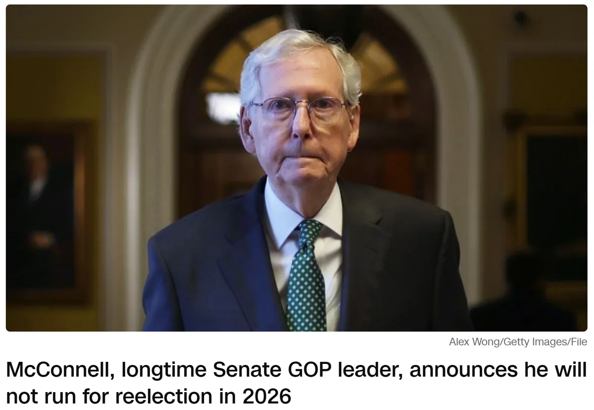 A man with white hair and glasses wearing a dark suit and green patterned tie stands in a formal hallway. The overlaid text…