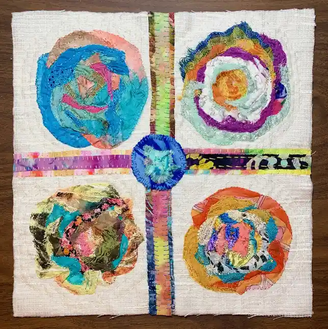 A handmade textile artwork displays four colorful, textured circular patches arranged in a square, each with a unique fabric…