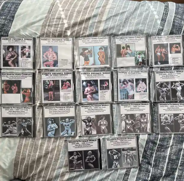 A collection of 'Women's Physique World' DVD cases, featuring various female bodybuilders in posing attire, are laid out in…