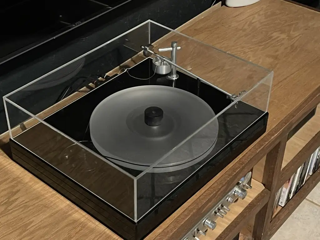 A modern turntable with a clear acrylic dust cover sits on a wooden media console, its platter empty and devoid of any vinyl…