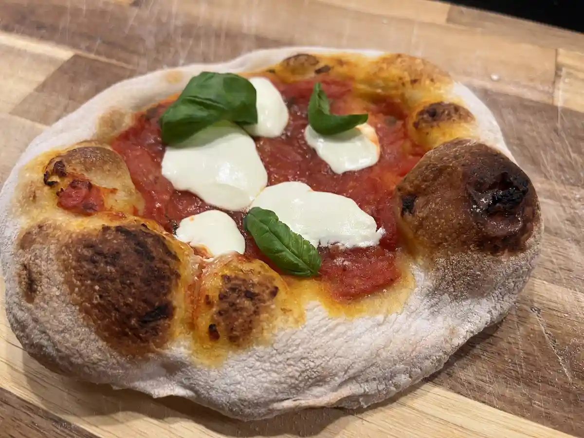 A freshly baked, rustic-style pizza with tomato sauce, mozzarella cheese, and basil leaves sits on a wooden cutting board…