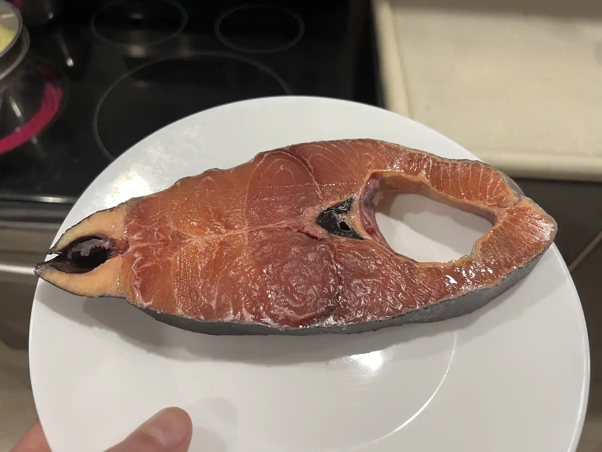 A raw salmon fillet sits on a white plate, its flesh showing a large, irregular hole in the center, resembling a missing eye…