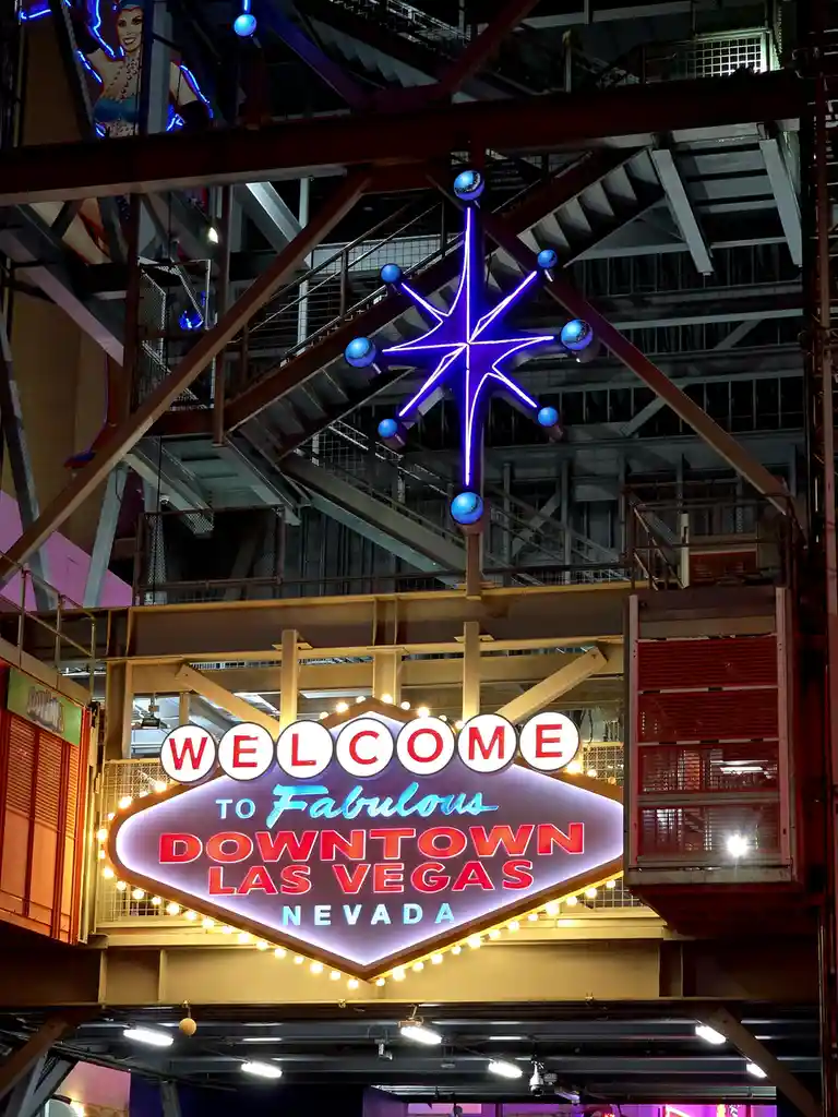 A brightly lit, iconic neon sign reads 'WELCOME TO Fabulous DOWNTOWN LAS VEGAS NEVADA' in red and blue lettering, framed by…