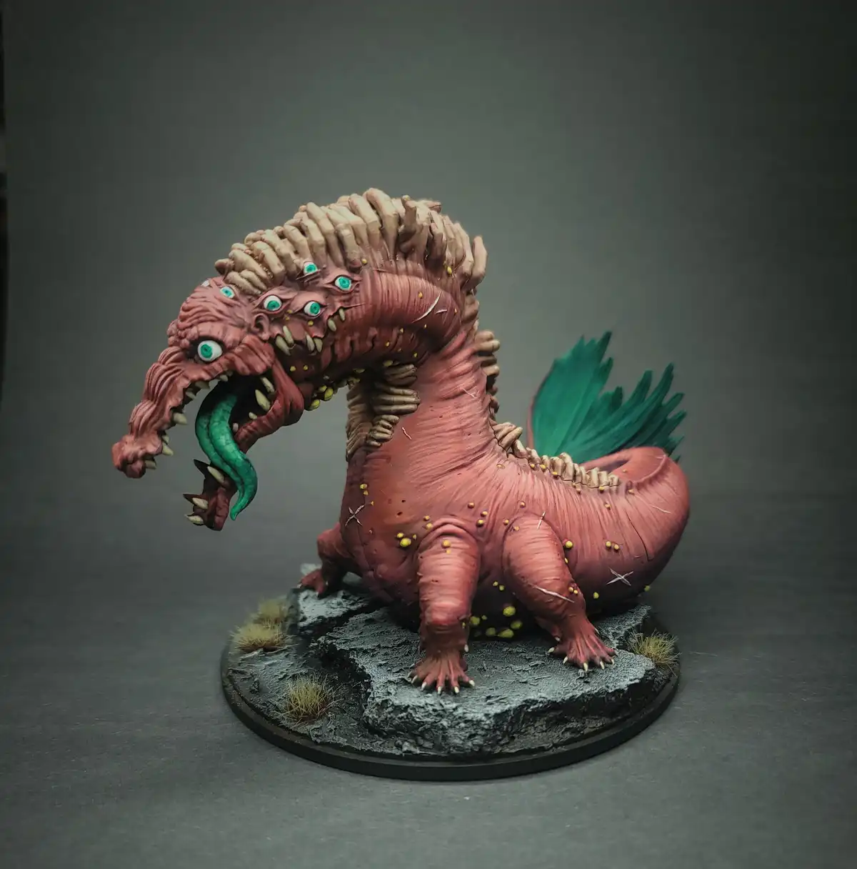A highly detailed, painted miniature of a grotesque, pinkish-red, multi-eyed monster with a long, spiky mane, sharp teeth…