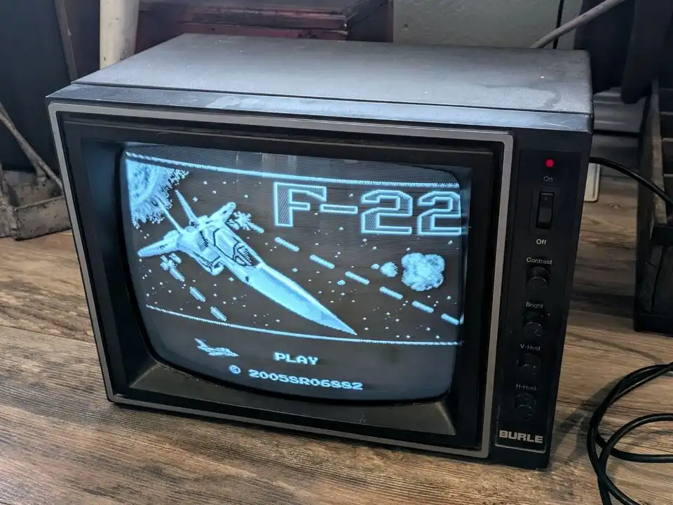 An old Burle brand CRT television displays a pixelated video game featuring a fighter jet labeled 'F-22' against a space…