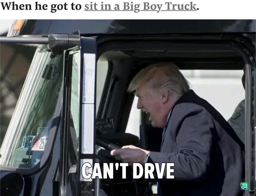 A man with blond hair and a gray suit is seated inside the driver's cabin of a large truck, gripping the steering wheel with…