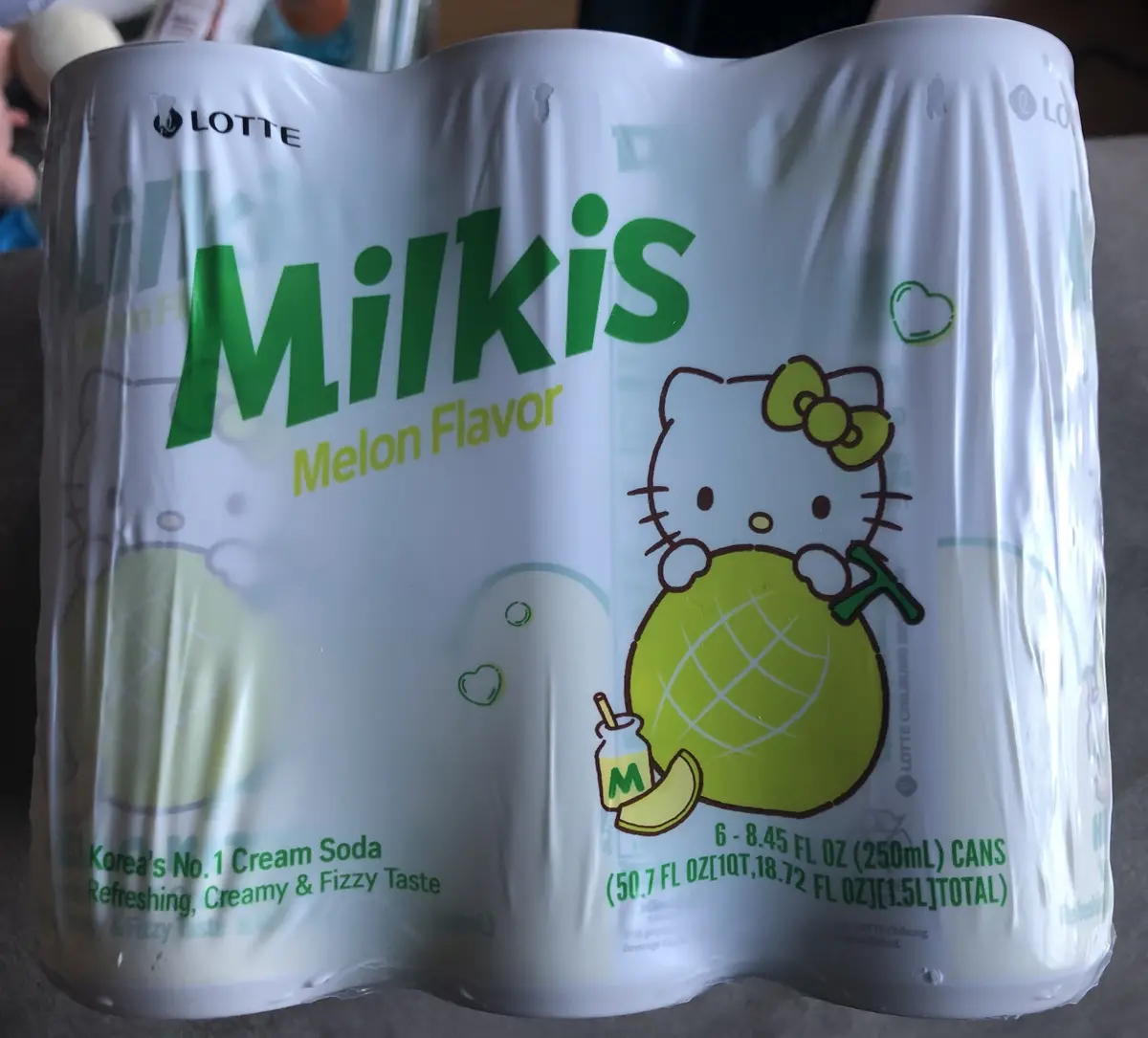 A close-up photo of a six-pack of Lotte Milkis Melon Flavor soda, featuring the Hello Kitty character holding a melon and a…