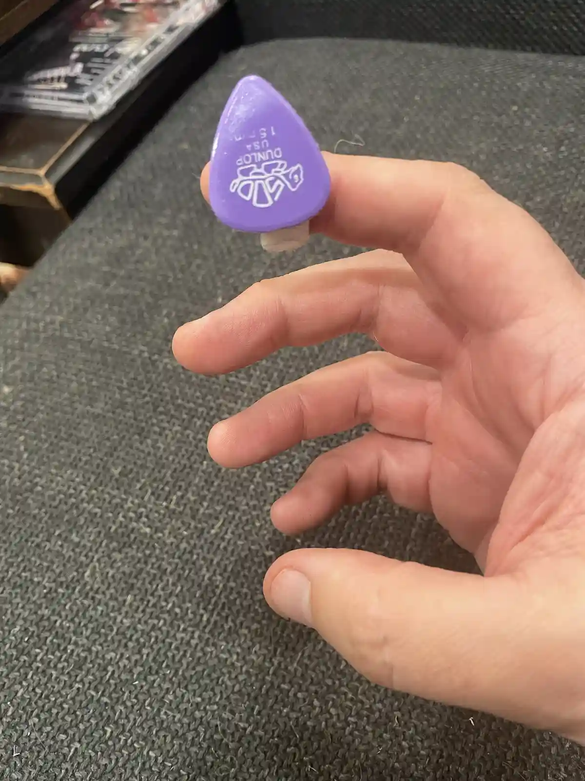A hand holds a purple Dunlop guitar pick, which is visibly taped to the tip of the index finger, with the text 'i'm not a…