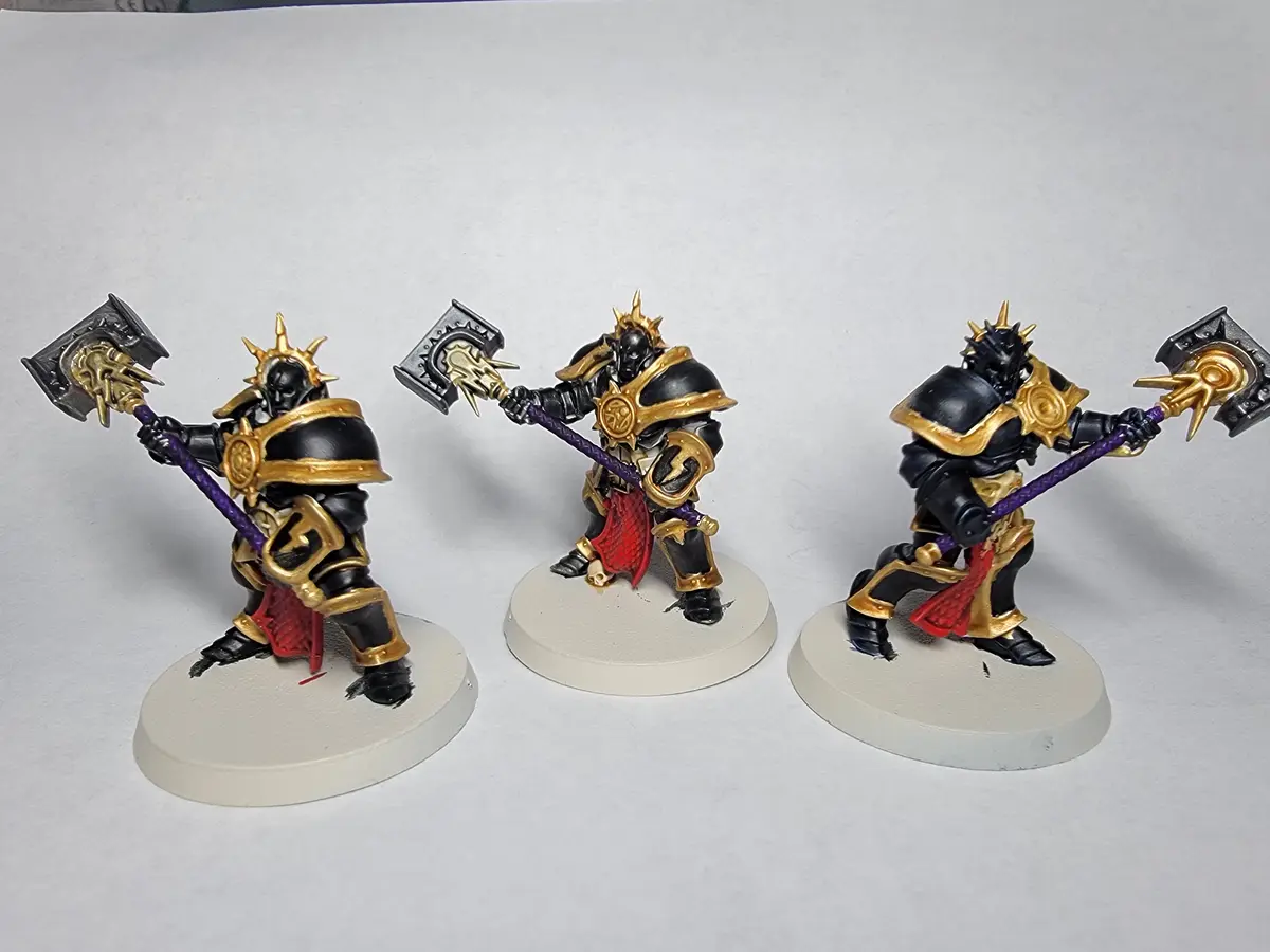 Three identical miniature figures of black-armored warriors with gold accents, each wielding a large purple-hafted axe…