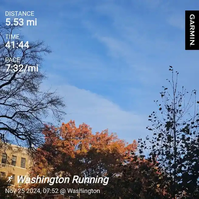 A Garmin fitness tracker screenshot overlaid on a photo of autumn trees and a blue sky, showing a 5.53-mile run completed in…