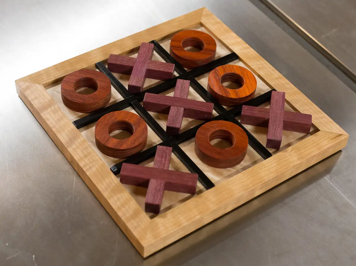A wooden tic-tac-toe board with dark red wooden pieces, showing a completed game where the 'X's have won by forming a…