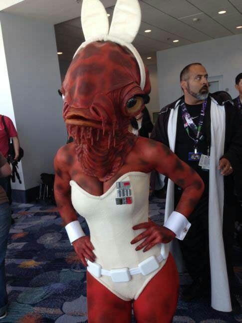 A person in a full-body, red-skinned alien costume with large white bunny ears and a white corset-like outfit stands with…