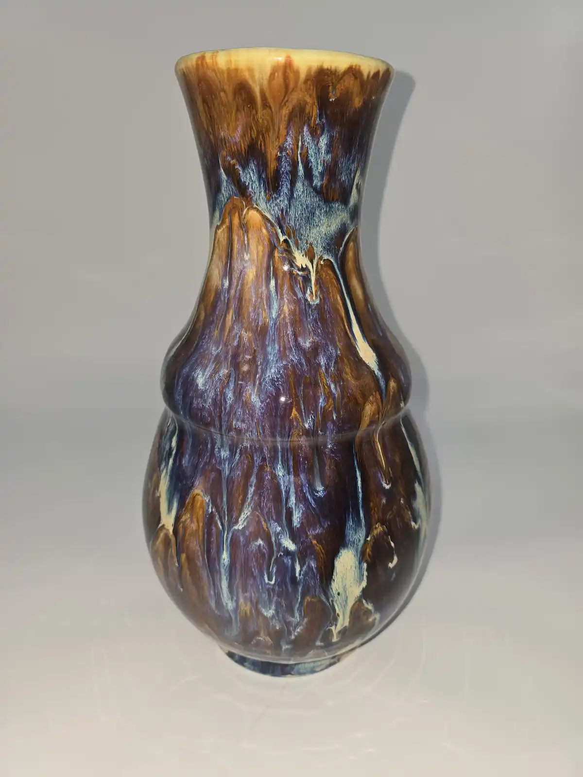 a ceramic vase with a glossy, multicolored glaze featuring brown, blue, and cream swirls that visually resemble a mountain…