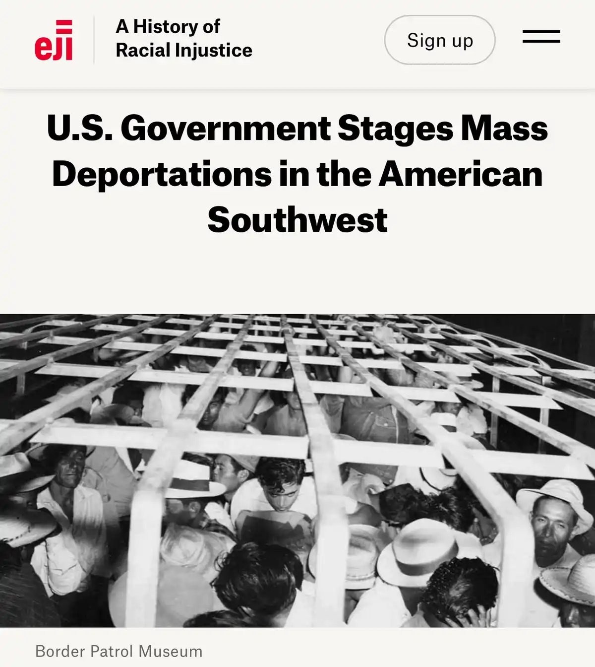 A black-and-white historical photo shows a large group of people, many wearing hats, crowded behind a wooden lattice…