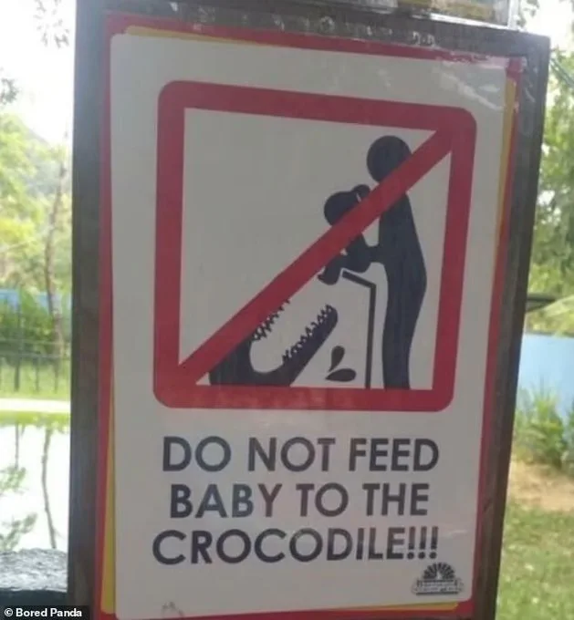 A warning sign shows a red prohibition symbol over a silhouette of a person feeding a baby to a crocodile. Below the symbol…