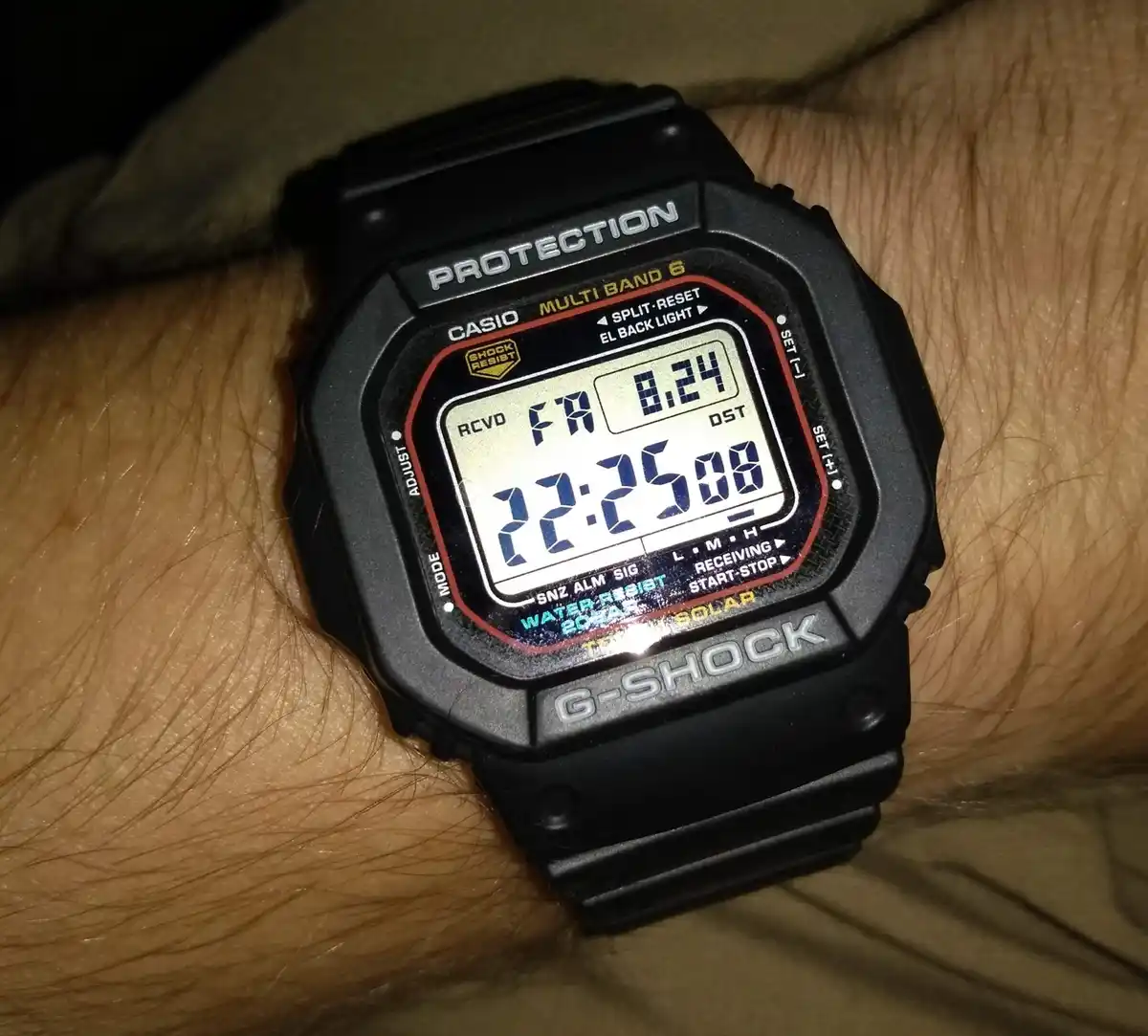A close-up photo of a black Casio G-Shock digital watch on a person's wrist, showing the time as 12:25:08, day as Friday…