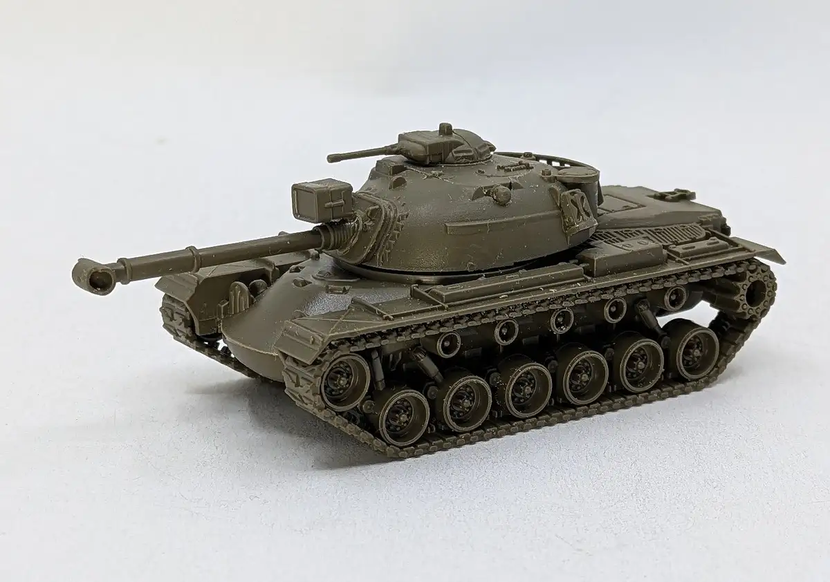 A detailed olive-drab model of a military tank is photographed against a plain white background. The tank has a long barrel…