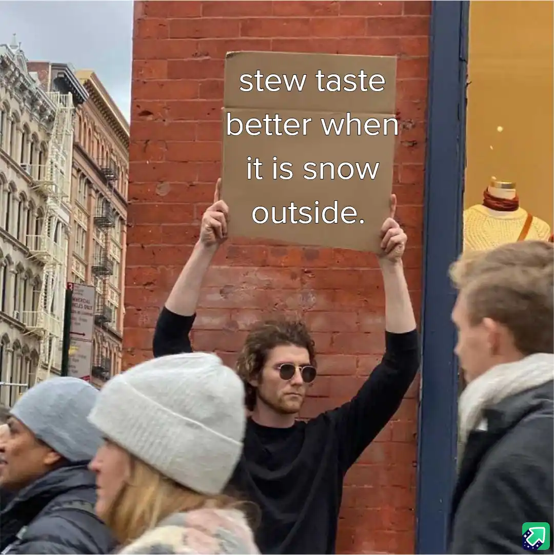 A man with curly hair and sunglasses holds up a cardboard sign in front of a brick wall, surrounded by pedestrians on a city…