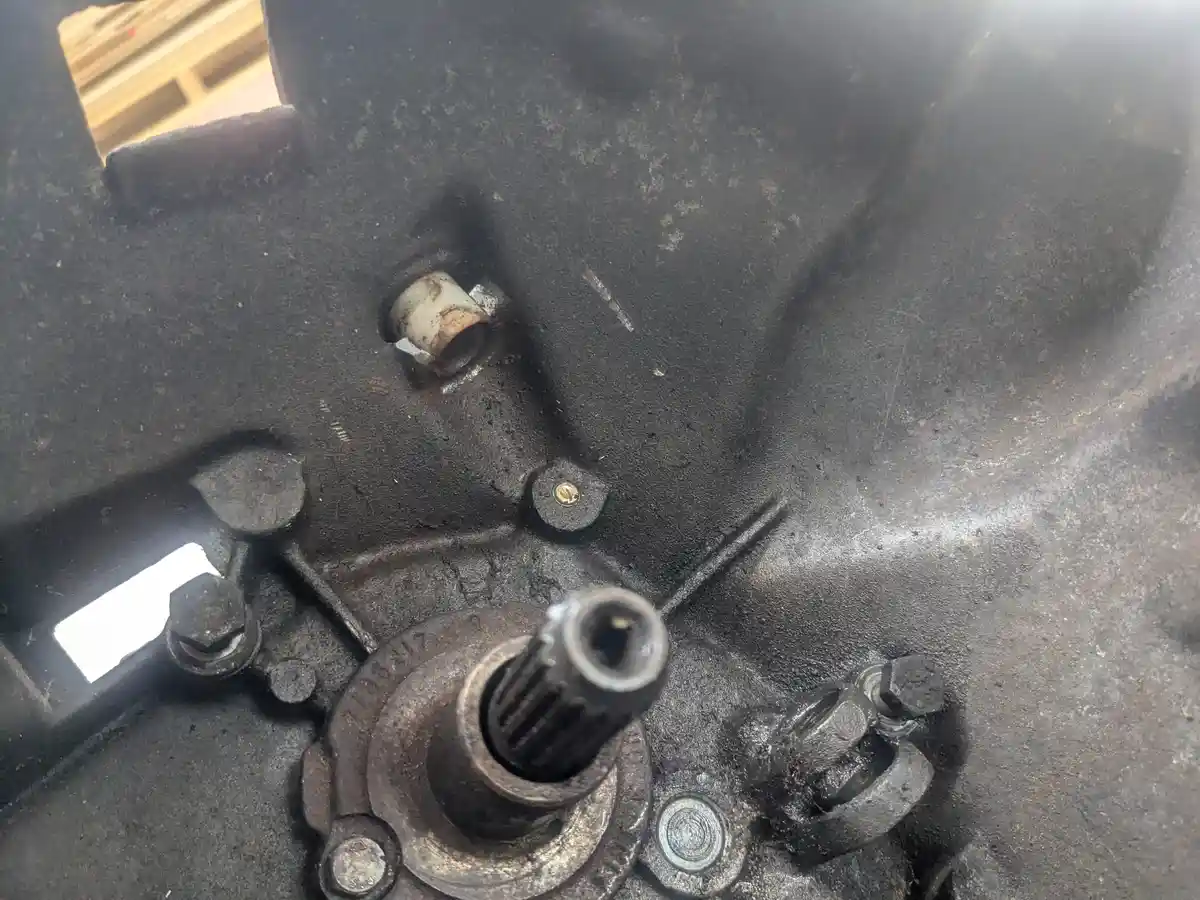 A close-up photo of a dirty, greasy mechanical engine part with bolts, a gear, and a small white tube, overlaid with the…