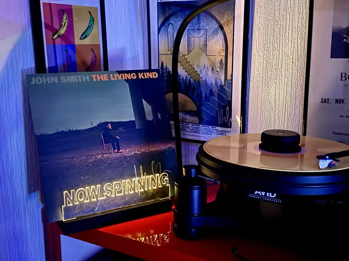 A vinyl record player sits on a red shelf next to a framed album cover for 'John Smith - The Living Kind'. The album cover…