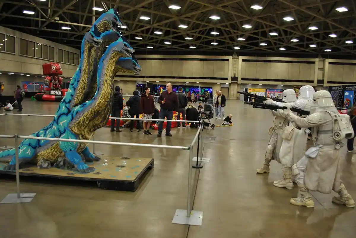 In a large convention hall, several people dressed as stormtroopers from Star Wars point their blasters at a large…