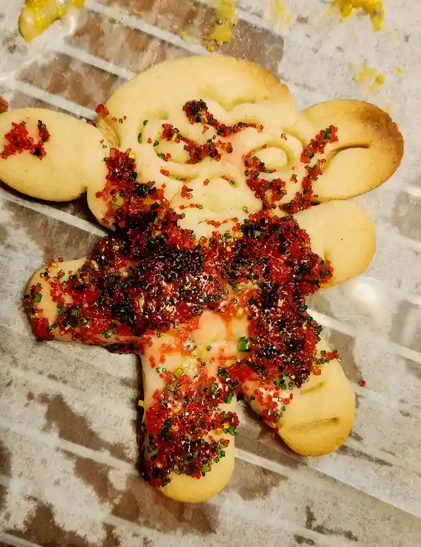 A gingerbread-style cookie shaped like a person with arms and legs, decorated with white icing and red, green, and gold…