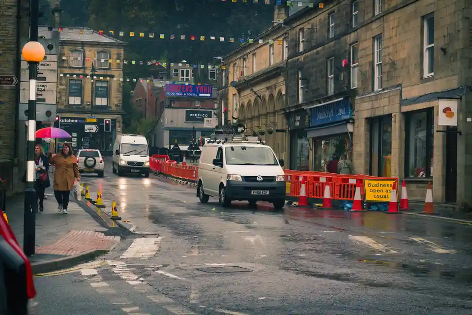 A wet, rainy street scene with pedestrians, cars, and storefronts, featuring a yellow sign that reads 'Business open as…