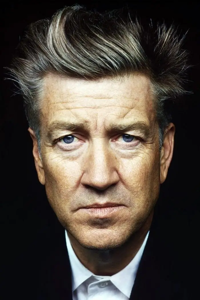 A close-up portrait of a middle-aged man with graying hair, intense blue eyes, and a stern, disappointed expression. He…